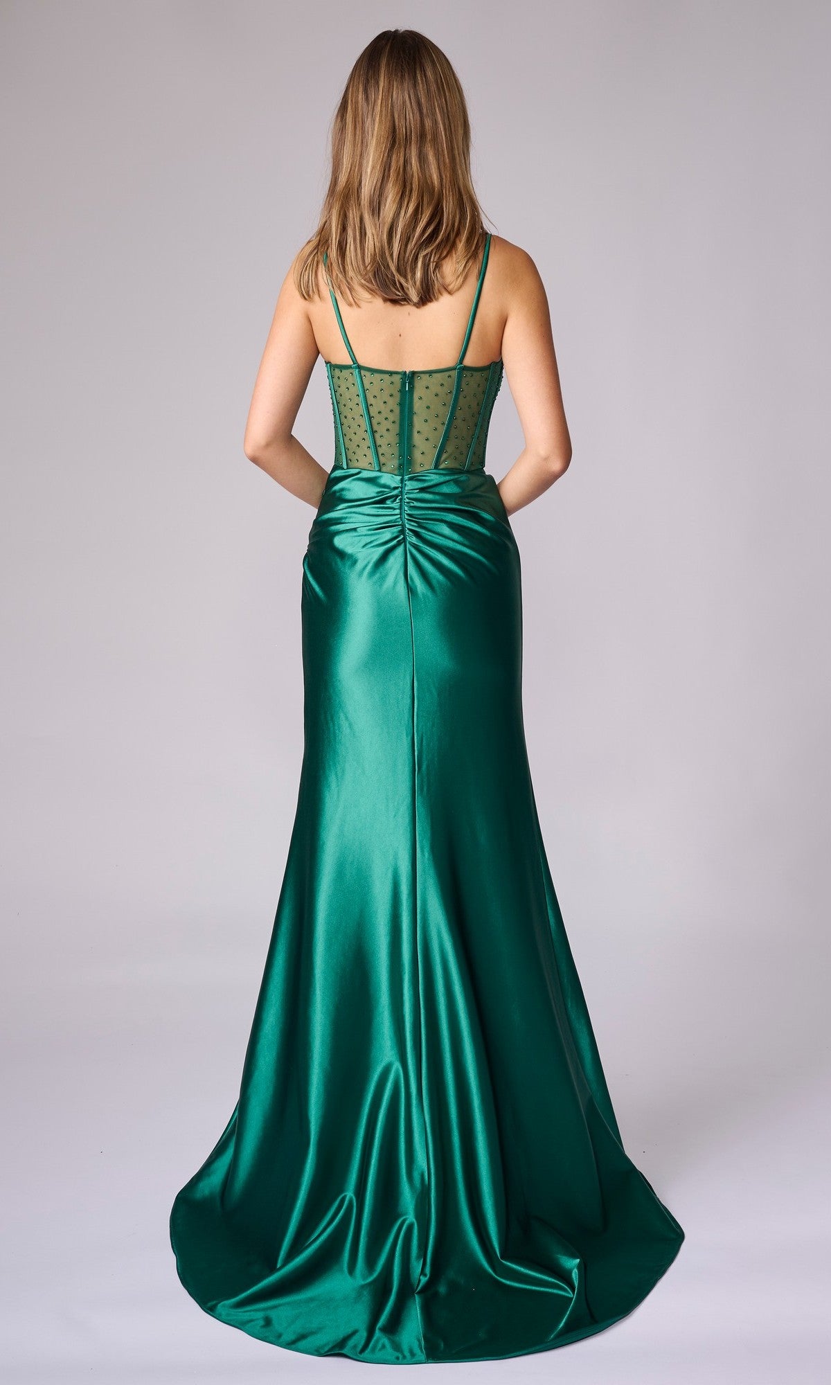 A woman faces away, wearing the Nina Canacci 5410—a floor-length emerald green formal dress with a fitted ruched back and sheer polka-dot bodice.